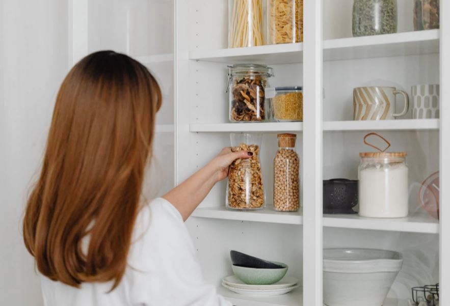 a-woman-in-white-shirt-holding-a-clear-glass-jar-a-shelf-full-of-clear-glass-jars-and-other-kitchen-necessities