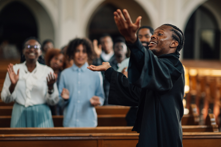 Preacher delivering a passionate sermon with his hands raised in the air as he speaks to the diverse congregation