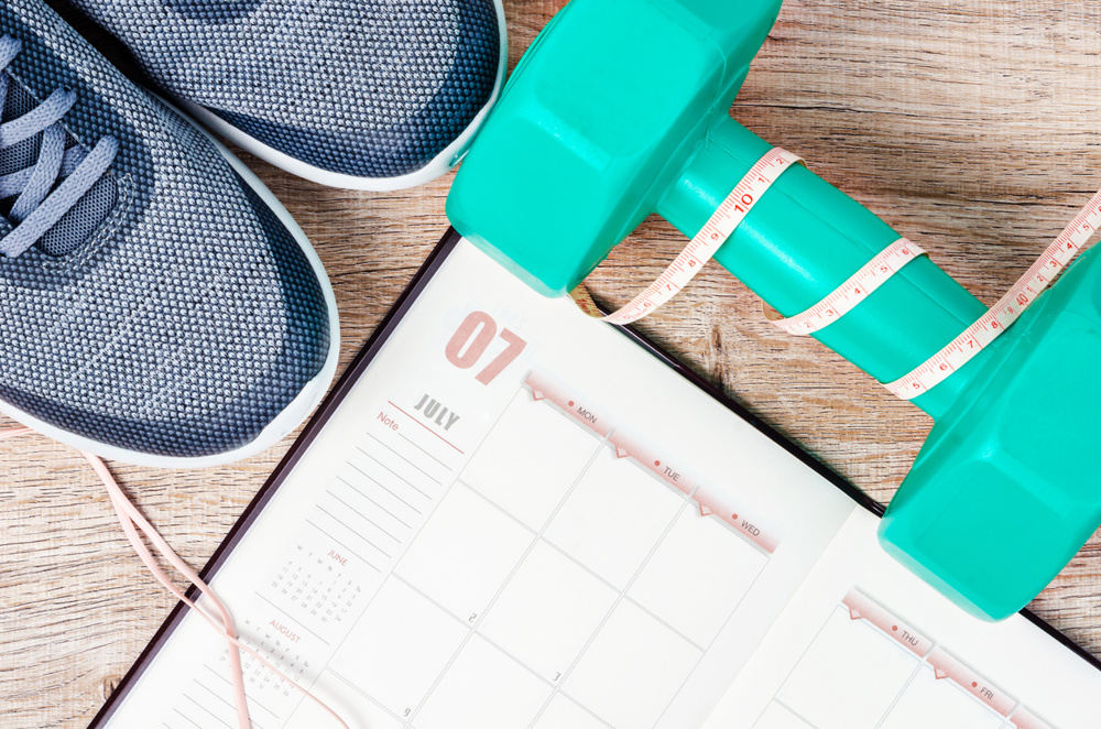 Calendar plan with green dumbbell and sneakers on wooden background. Workout plan concept