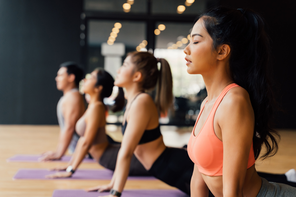 Group of people doing yoga upward facing dog pose on mats at yoga studio