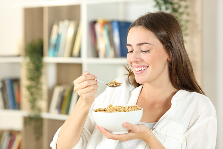 Happy woman eating cereals for breakfast at home
