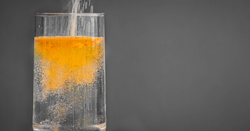 Powdered orange drink mix being poured into a clear glass of water
