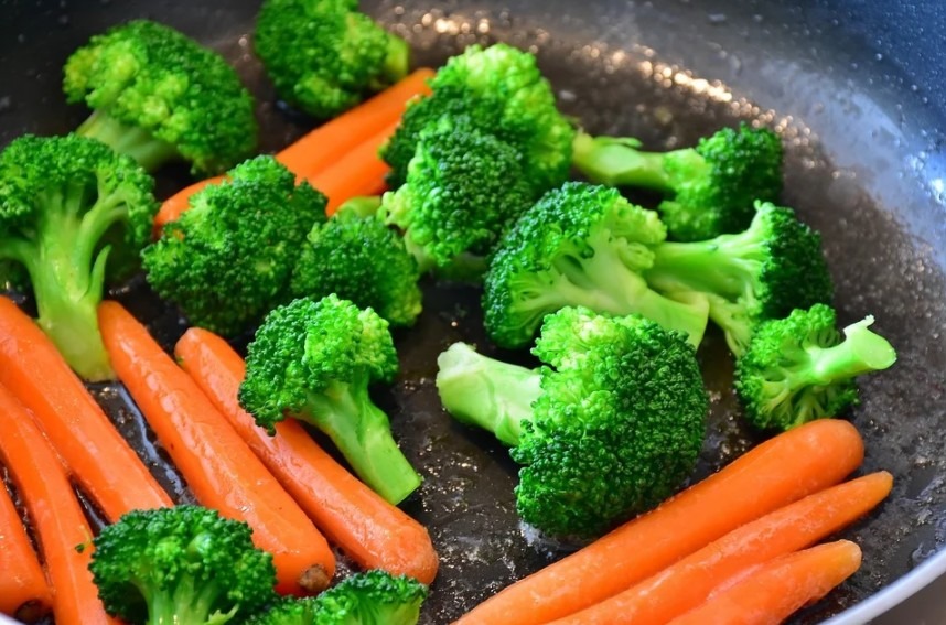 carrots and broccoli being sautéed in a pan