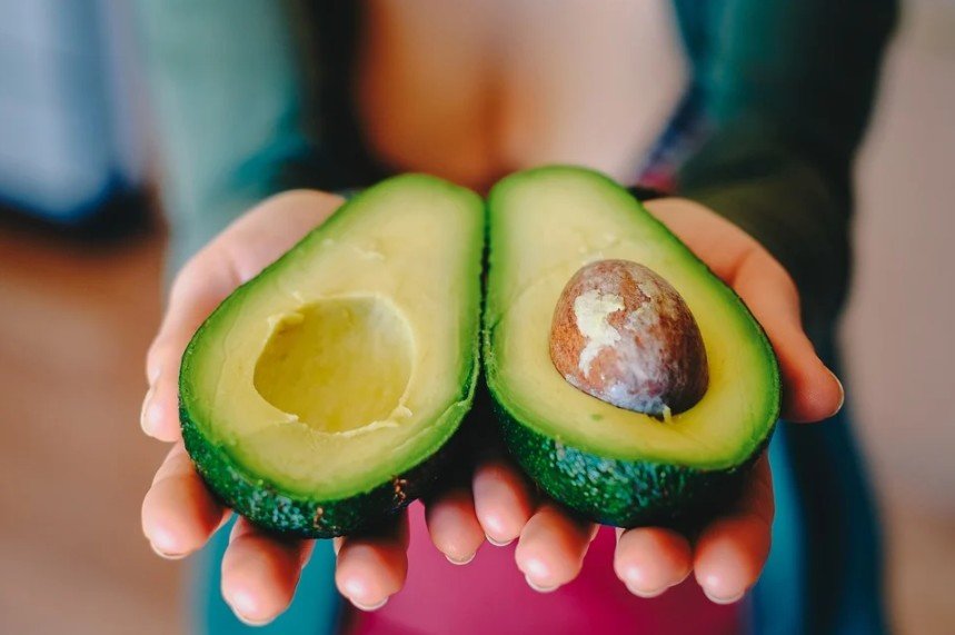 a pair of hands holding up the two halves of an avocado up to the camera