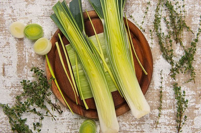 An image showing leeks cut in the middle on a wooden platter.