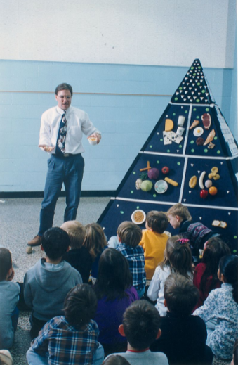 Image of a man explaining a food guide pyramid to people.