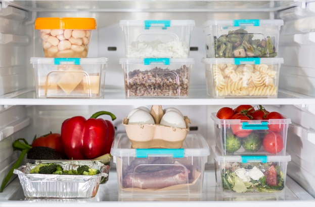 Open fridge with plastic food containers and vegetables