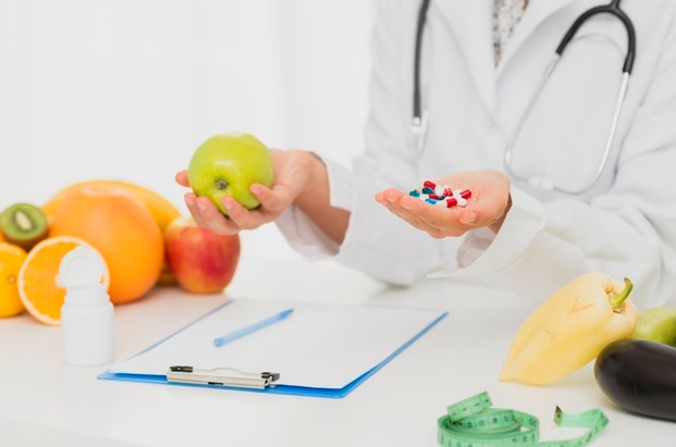 a doctor with pills in one hand, and fresh fruits in the other