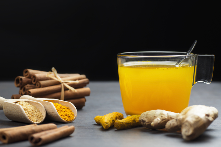 Herbal ginger and turmeric tea in glass cup with ginger root, dry turmeric, cinnamon sticks