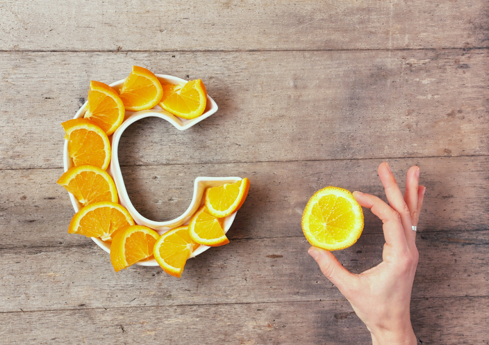 Vitamin C or Ascorbic acid nutrient in food concept. Plate in shape of letter C with orange slices and woman's hand with citrus making sign OK on wooden background. Flat lay or top view.