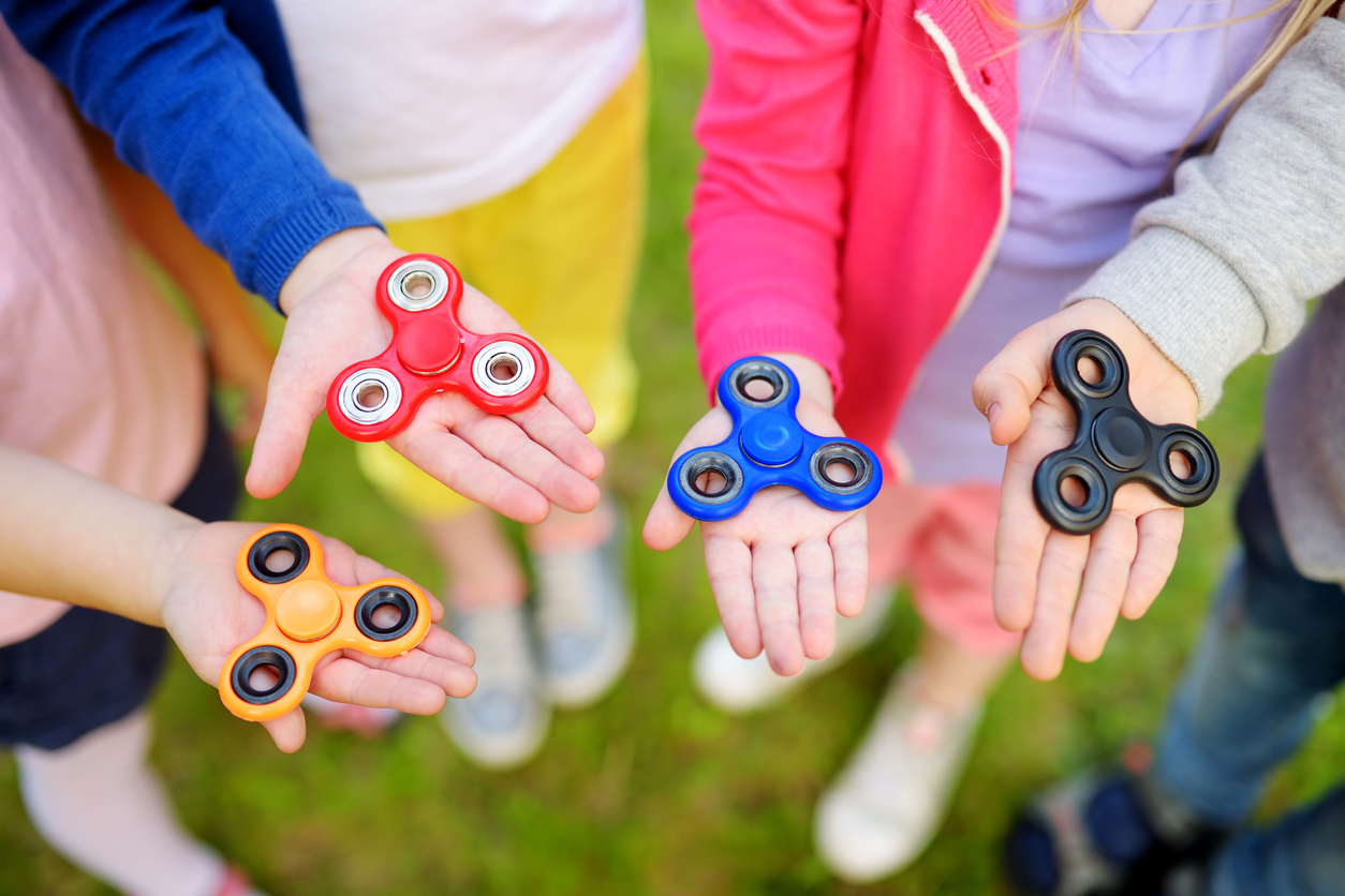 Four school children playing with fidget spinners on the playground
