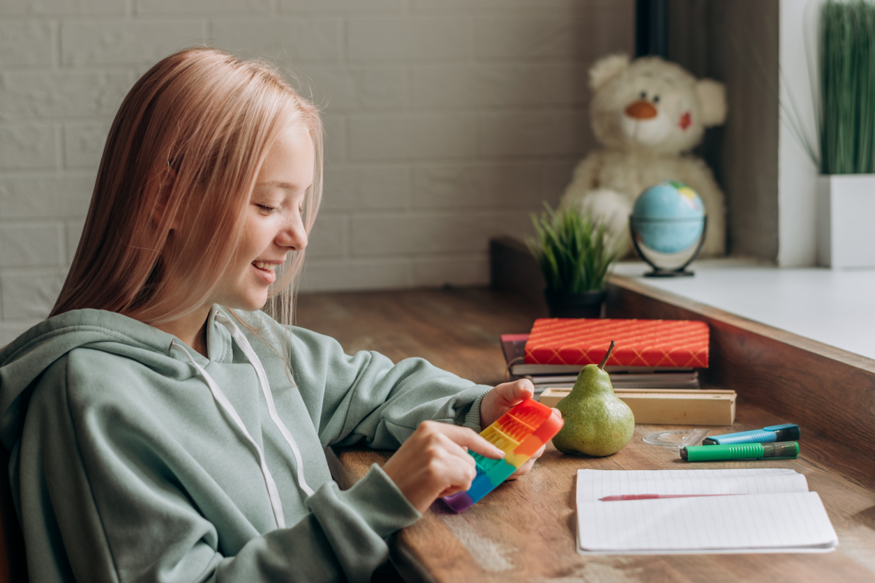 a teenage girl playing with a colorful pop-it fidget toy while studying at home