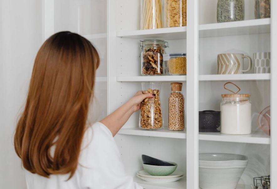 a-woman-in-white-shirt-holding-a-clear-glass-jar-a-shelf-full-of-clear-glass-jars-and-other-kitchen-necessities